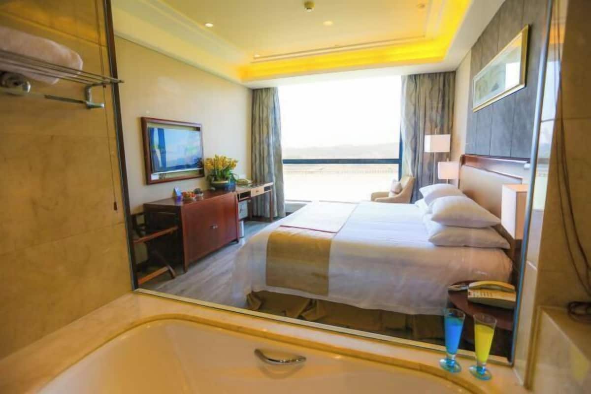 A hotel room with a large bed, a desk, a chair, a TV, and a view of the sea.