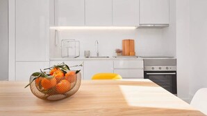A modern kitchen with white cabinets, a stainless steel stove, and a wooden table with a basket of oranges. - 2 Classic Apartments by HostWise (Porto)