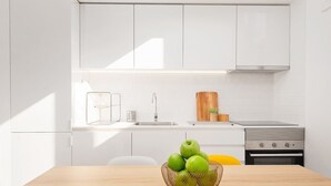 A modern kitchen with white cabinets, a stainless steel sink, a wooden cutting board, and a basket of green apples on the table.