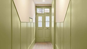 A hallway with green walls, a patterned rug, and a double door with windows.