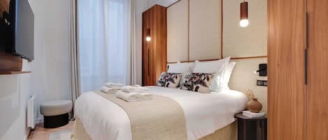 Une chambre à coucher moderne avec un grand lit, une table de chevet, un téléviseur fixé au mur et une armoire en bois.