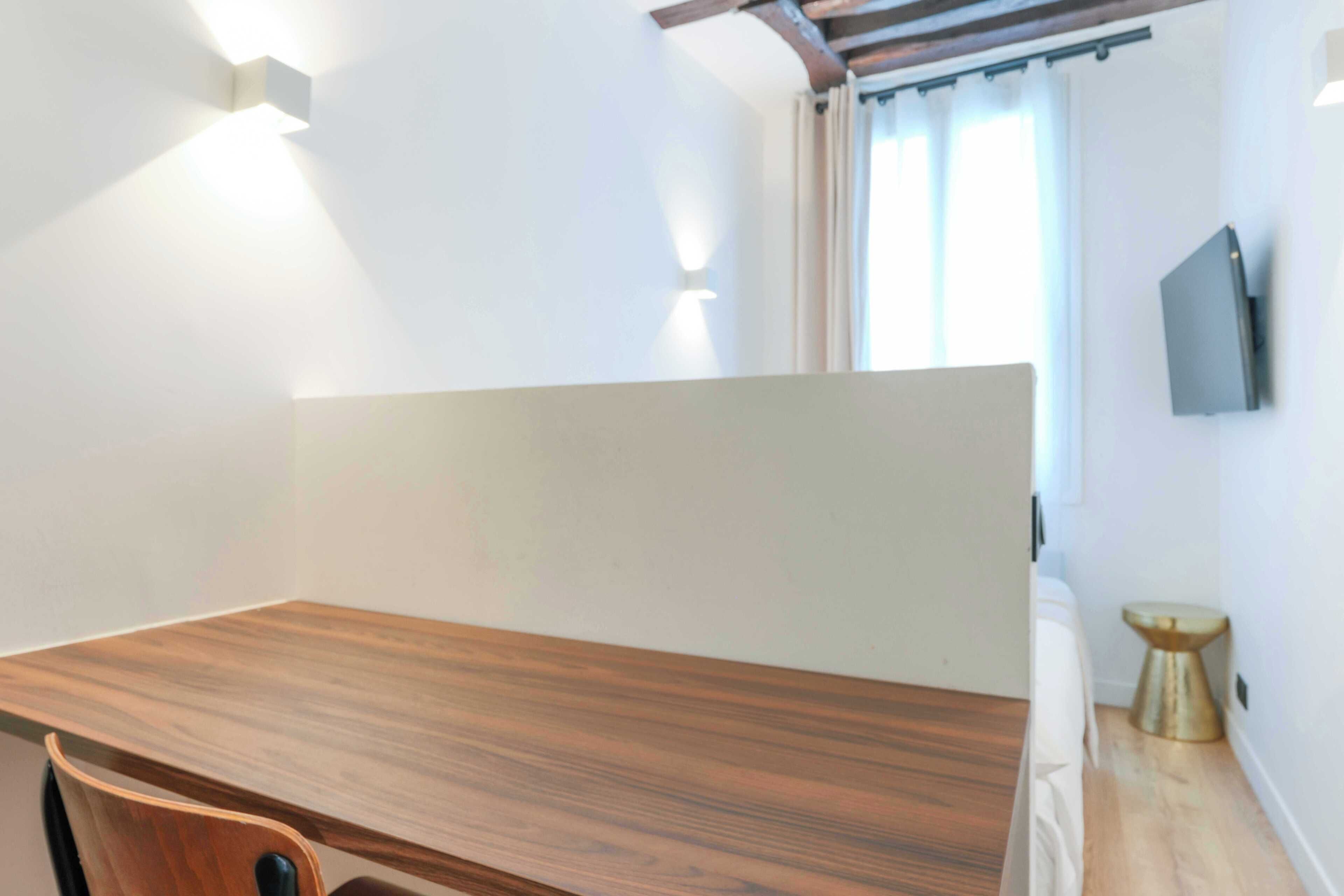A modern room with a wooden desk, a small stool, and a TV mounted on the wall.