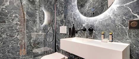 A modern bathroom with a marble backsplash, a white sink, and a wooden cabinet.