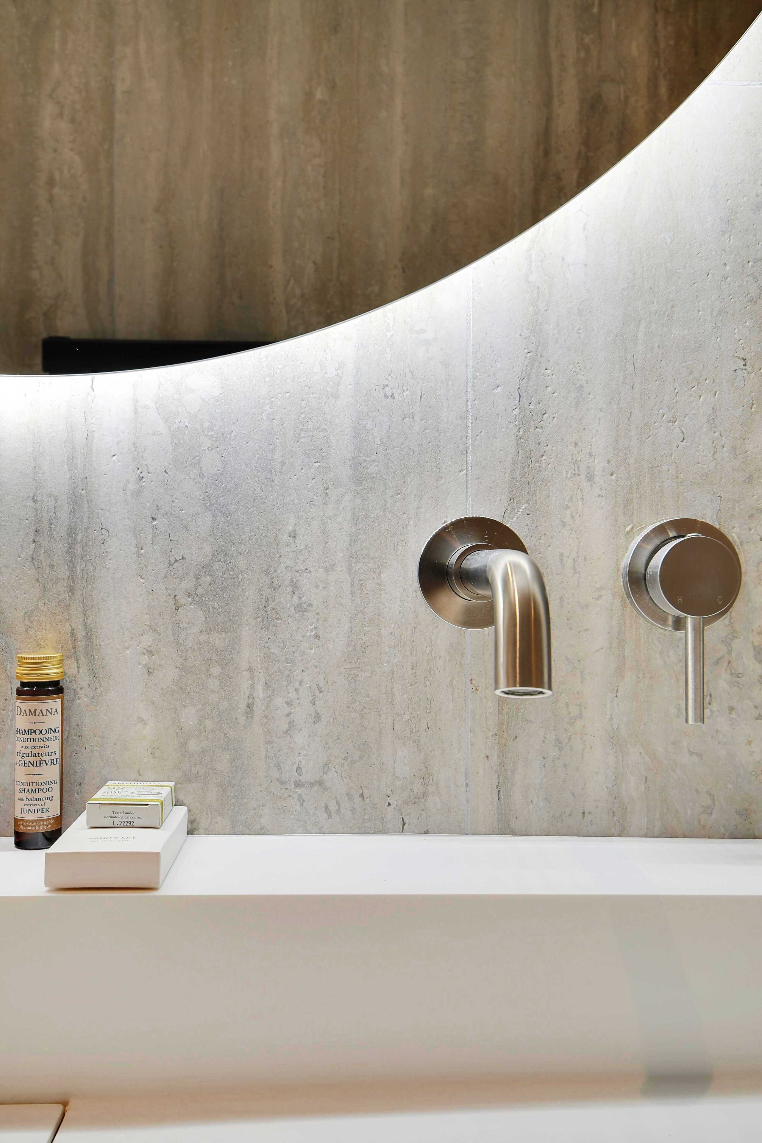 A modern bathroom with a curved wall, a white sink, and two chrome faucets.