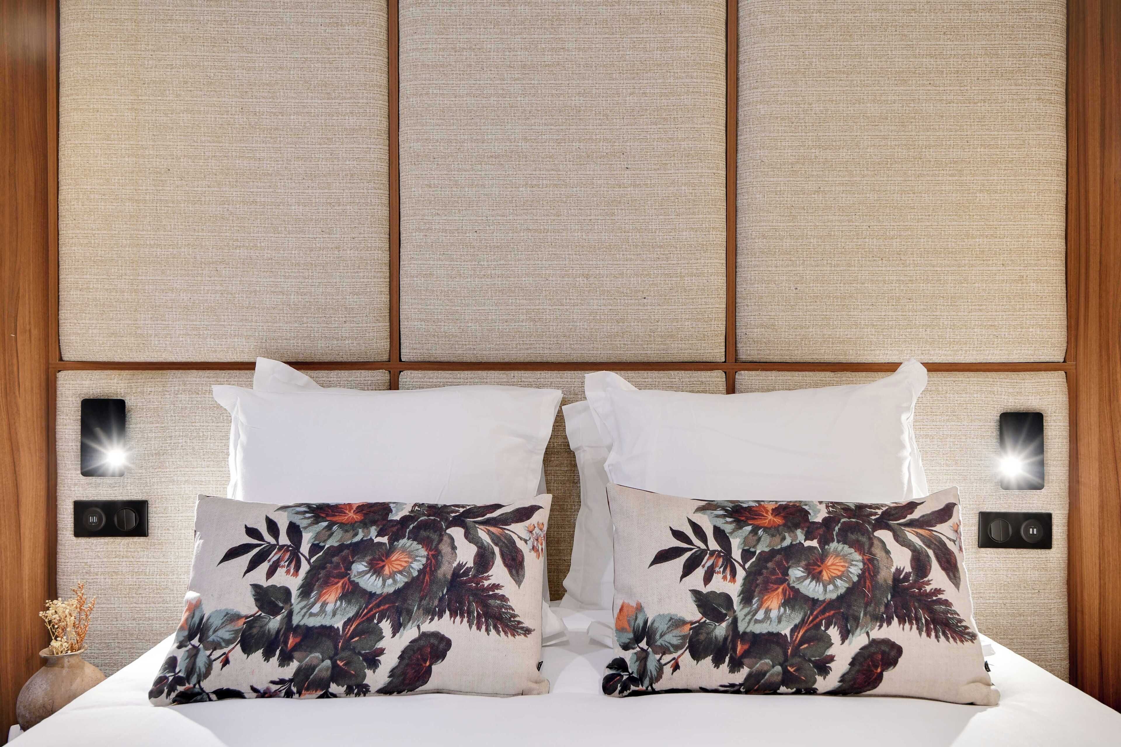A neatly made bed with white linens and two decorative pillows with a floral pattern.