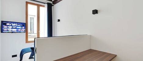 A modern room with a wooden desk, a television mounted on the wall, and a window with curtains.