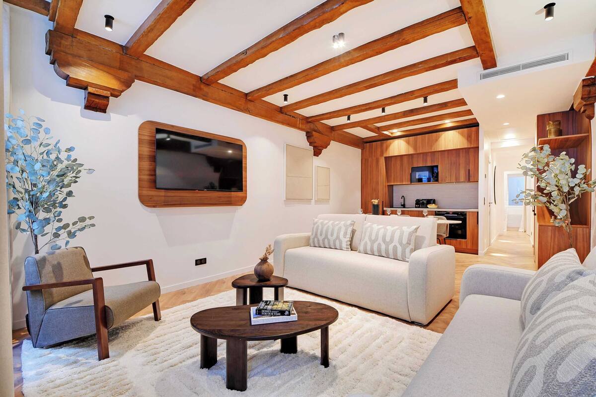 Ein modernes Wohnzimmer mit einem weißen Sofa, einem Holztisch und einem an der Wand montierten Fernseher.
