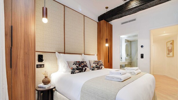 Une chambre d’hôtel moderne avec un grand lit, des panneaux de bois, une petite table d’appoint et une lampe de chevet.