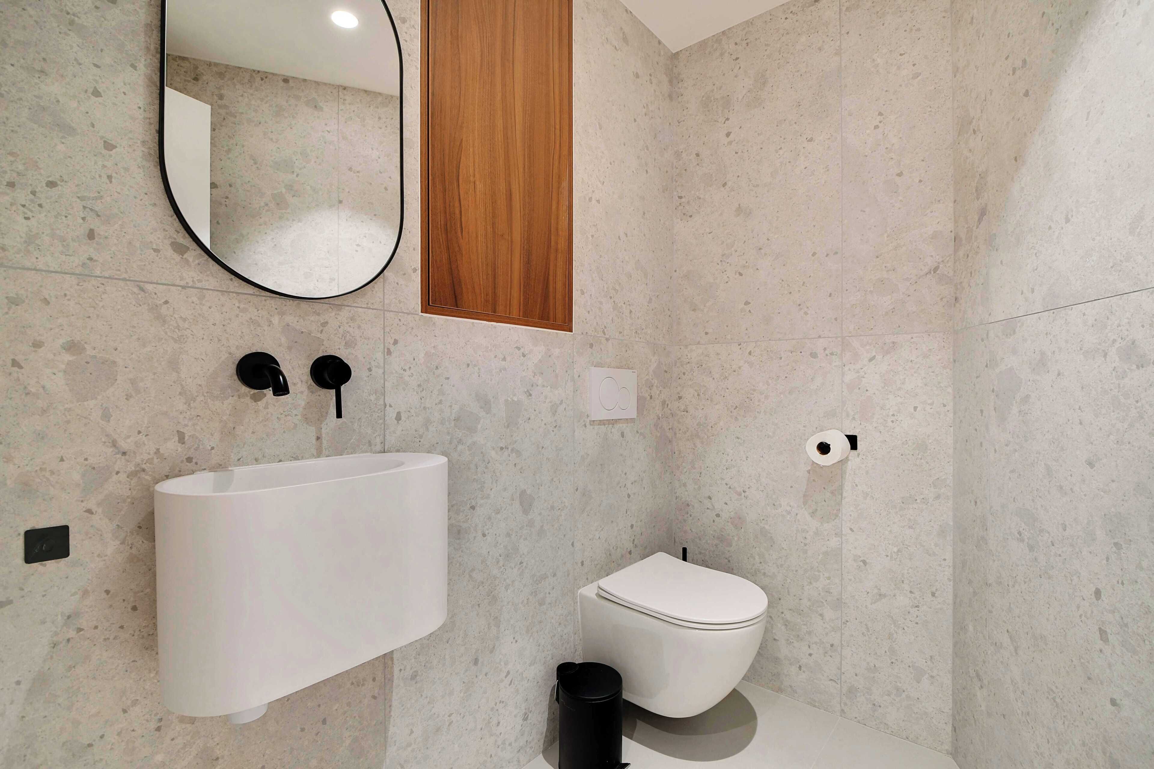 A modern bathroom with a freestanding sink, a toilet, a mirror, and a wooden panel above the mirror.