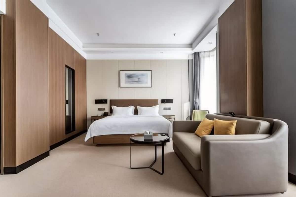 A hotel room with a bed, a sofa, a small table, and a window.