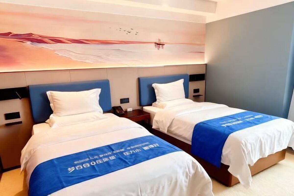 Ein Hotelzimmer mit zwei Betten, einem großen Gemälde an der Wand und einer blauen Tagesdecke mit Aufschrift.