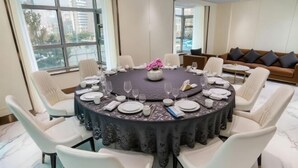 A round dining table set for six with white chairs, a vase of pink flowers, and a dark tablecloth. - Qinhuangdao Haishanghai International Hotel (Qinhuangdao)