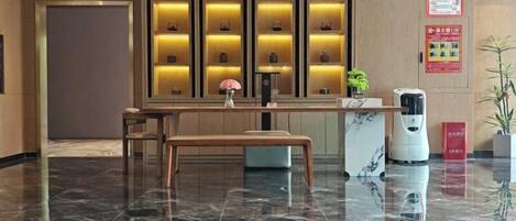 Zona de recepción de un hotel con piso de mármol, mostrador de recepción, una banca y una pared con vitrinas iluminadas.