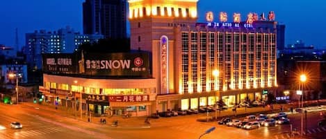 Un hotel de varios pisos con señalización iluminada, una entrada destacada y un estacionamiento.