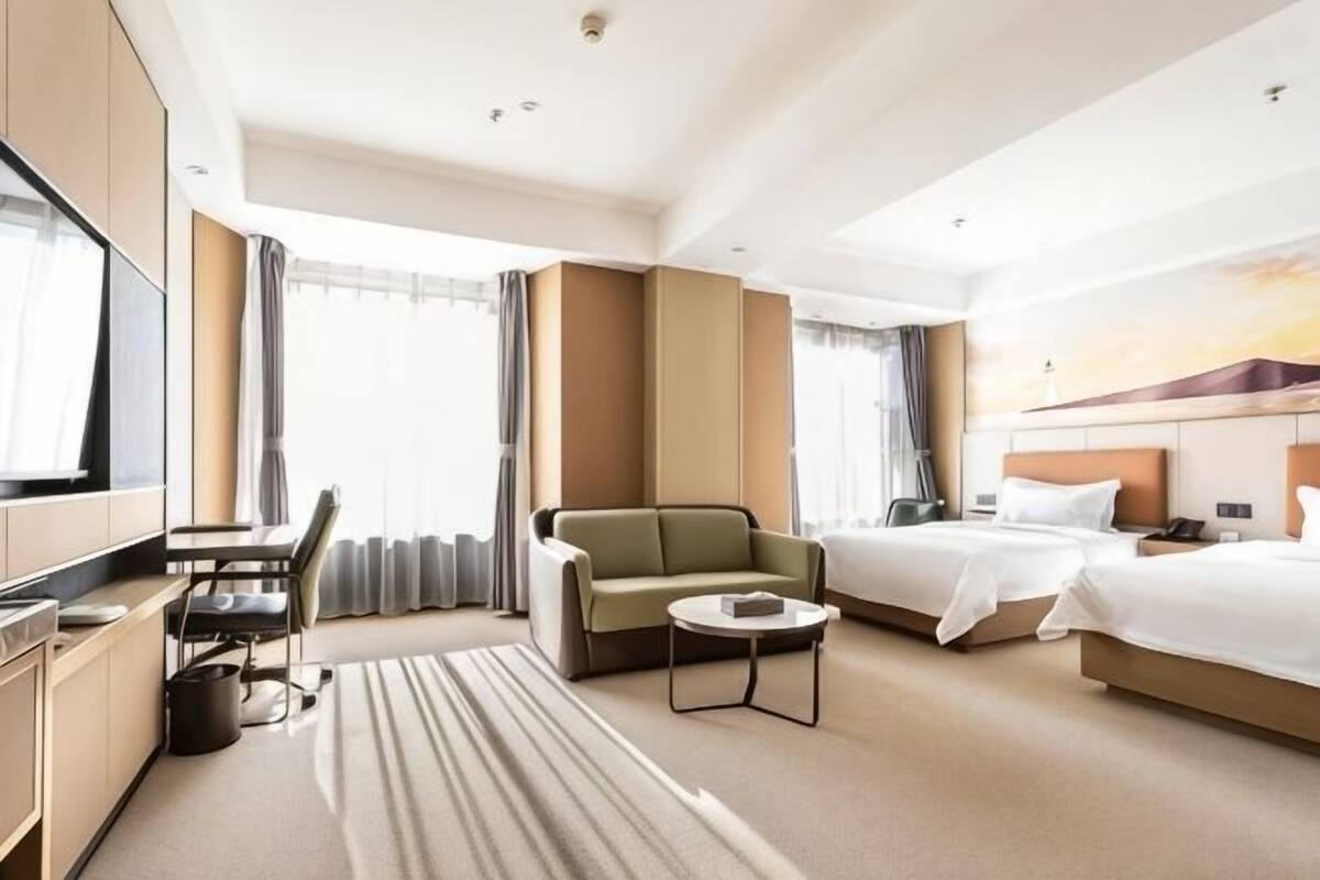 Ein Hotelzimmer mit einer Couch, zwei Betten, einem Fernseher, einem Schreibtisch und Blick ins Freie.