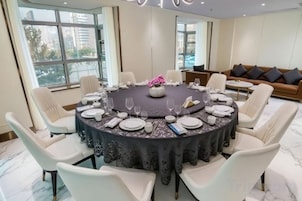 Mesa redonda para seis personas, con sillas blancas, un centro de mesa floral y mantel oscuro.