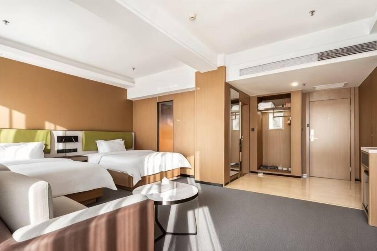 Ein Hotelzimmer mit zwei Betten, einem Schlafsofa, einem kleinen Tisch und einem begehbaren Kleiderschrank.
