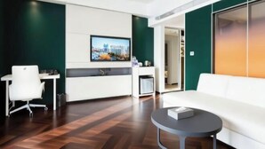 A modern hotel room with a wooden floor, a white sofa, a small round table, a desk with a chair, and a TV mounted on the wall. - Qinhuangdao Haishanghai International Hotel (Qinhuangdao)