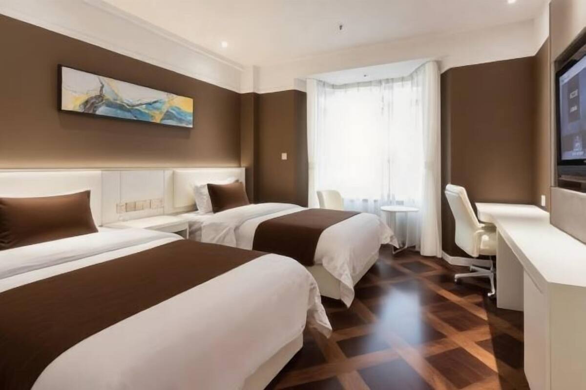 Ein Hotelzimmer mit zwei Betten, einem Schreibtisch, einem Sessel, einem Fernseher und einem Gemälde an der Wand.