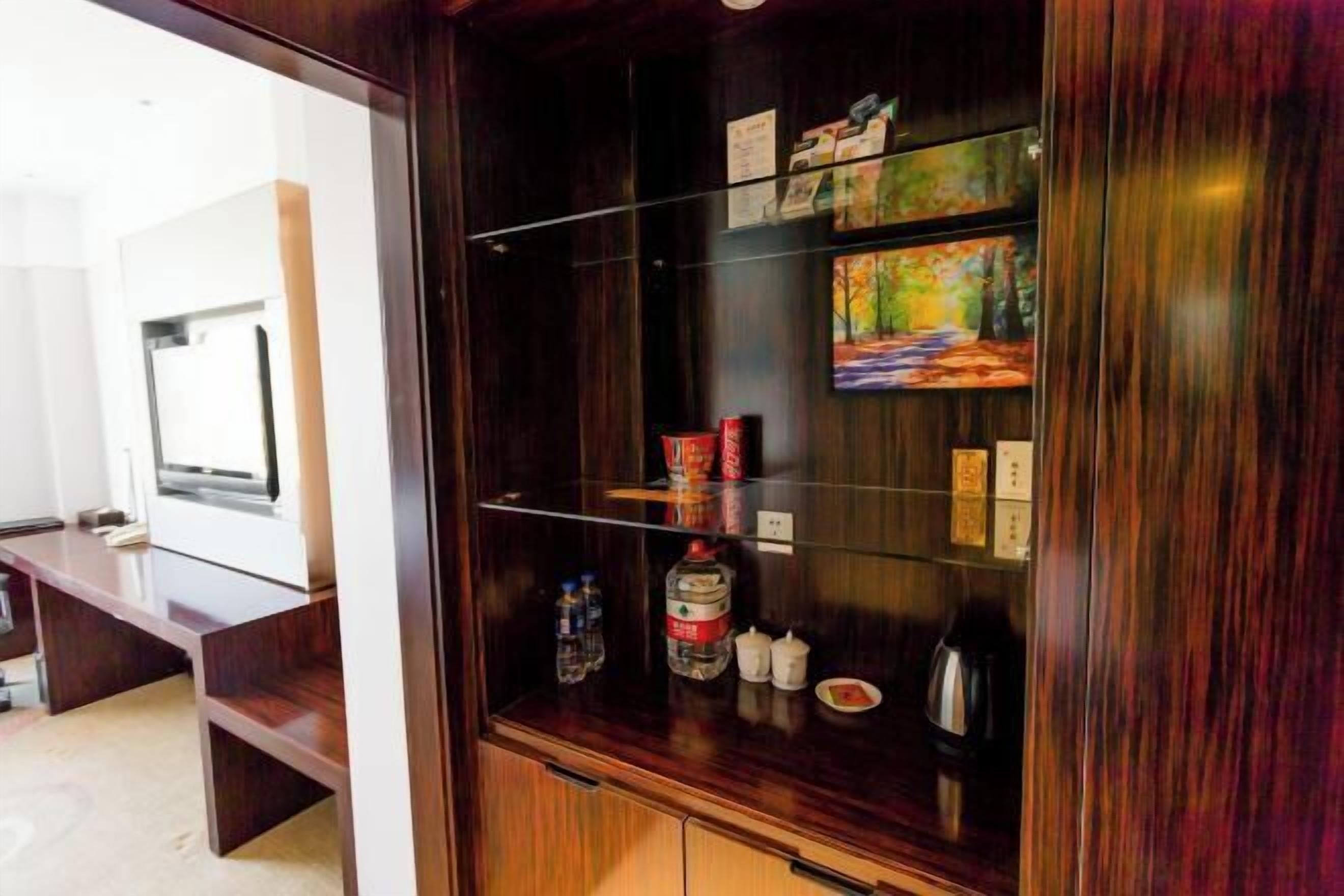 A wooden cabinet with glass doors, containing a painting, a water bottle, and a coffee maker.