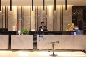 Un mostrador de recepción de hotel con un empleado uniformado, una planta y un cartel.
