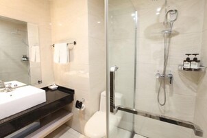 Un baño moderno con ducha envuelta en vidrio, un lavamanos blanco y un inodoro.