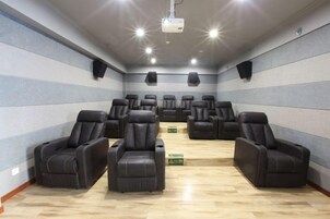 Una sala con varias sillas reclinables dispuestas en filas, un proyector en el techo y altavoces en las paredes.