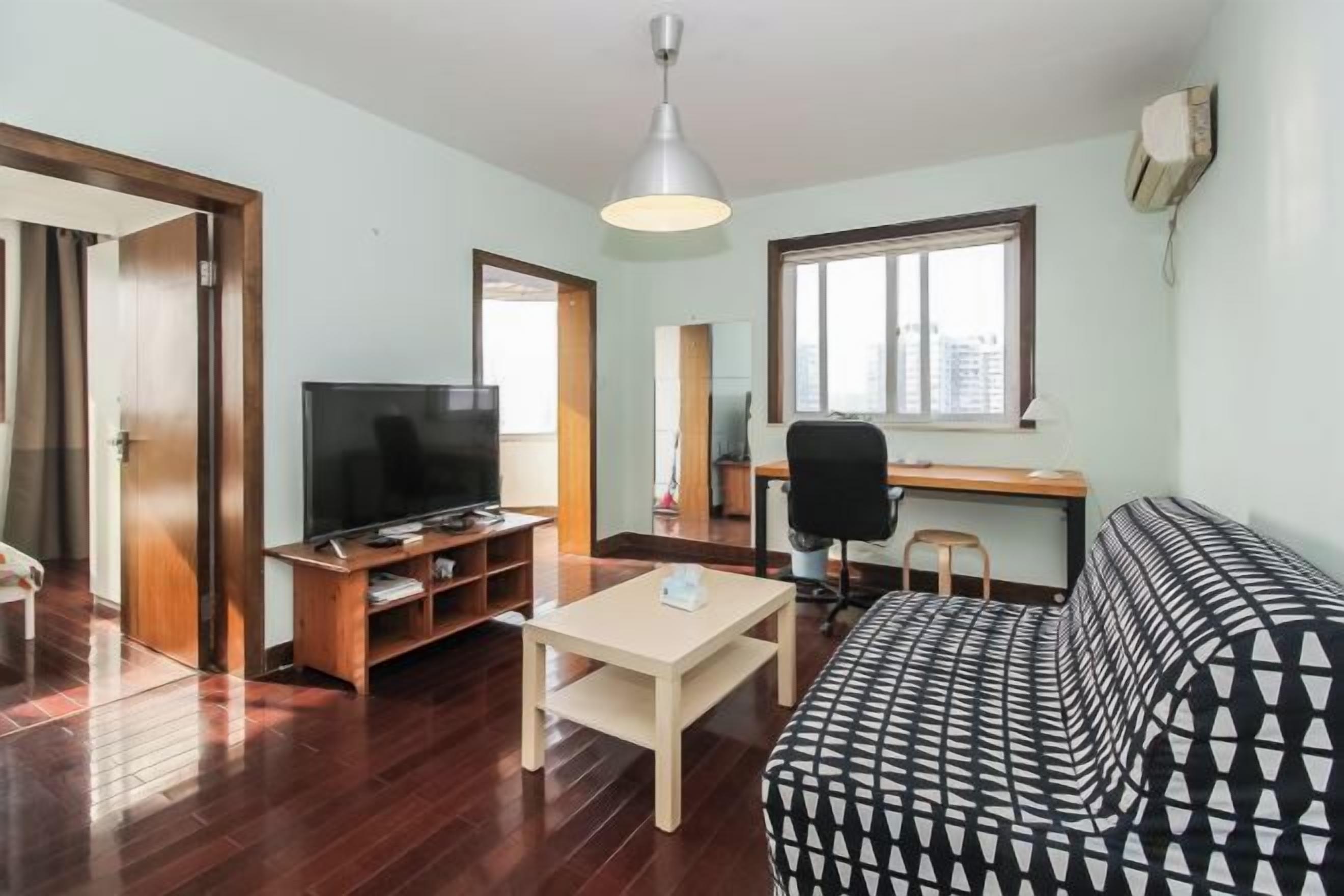 Uma sala de estar com sofá, televisão, escrivaninha e uma cadeira.
