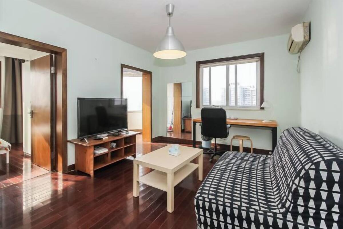Una sala de estar con televisor, muebles de madera, un sofá, un escritorio y una ventana.