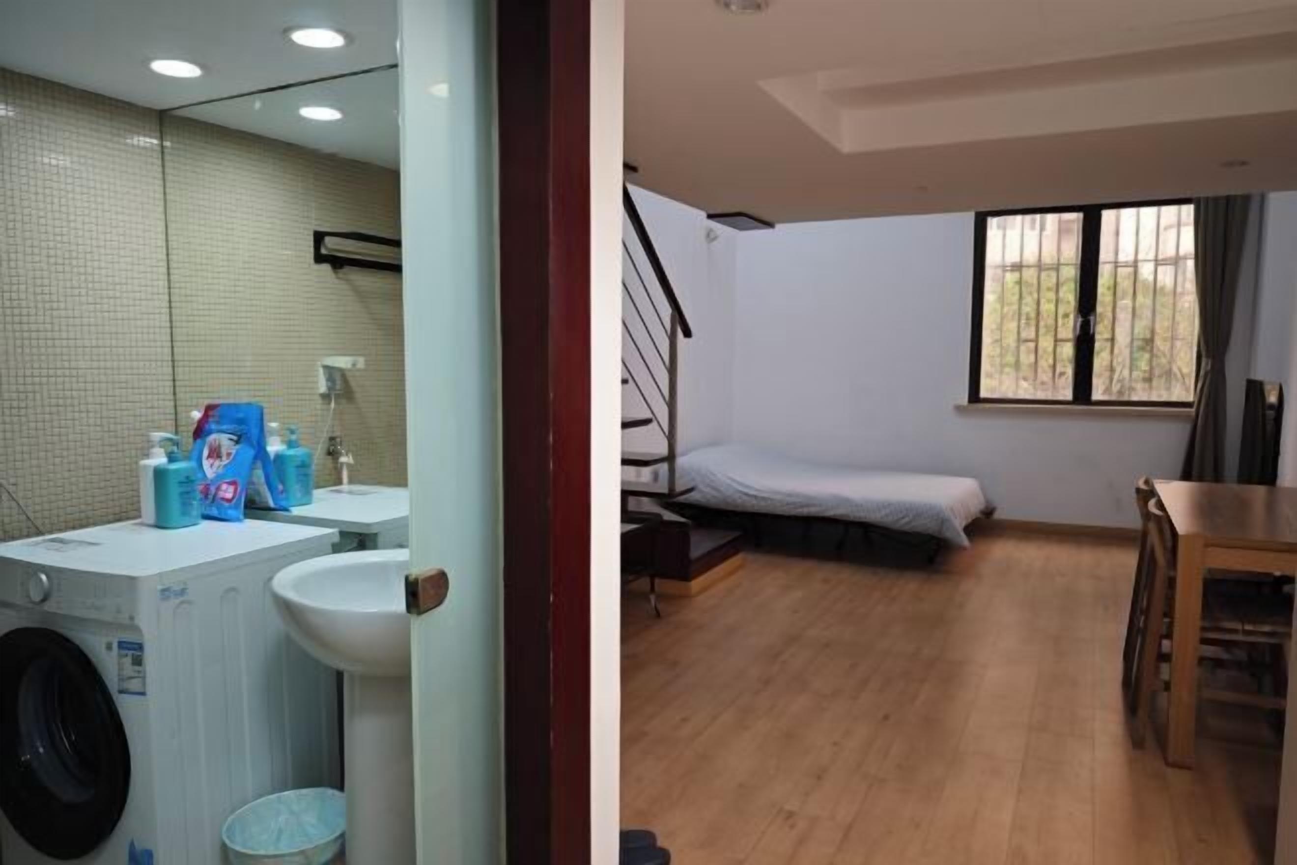 A room with a bed, a window, a table, and a washing machine.
