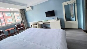 Habitación de hotel con una cama grande, un escritorio, un televisor de pantalla plana, una silla y una ventana con vistas a edificios.