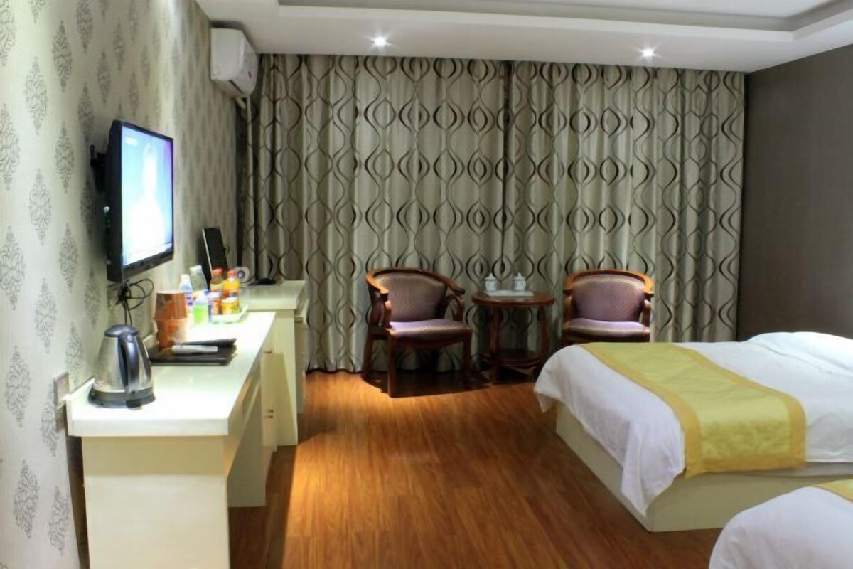 Ein Hotelzimmer mit einem Bett, einem Schreibtisch mit Wasserkocher, zwei Stühlen, einem Fernseher und gemusterten Vorhängen.