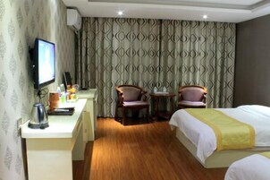 Habitación de hotel con cama, escritorio con tetera, dos sillas, televisor y cortinas estampadas.