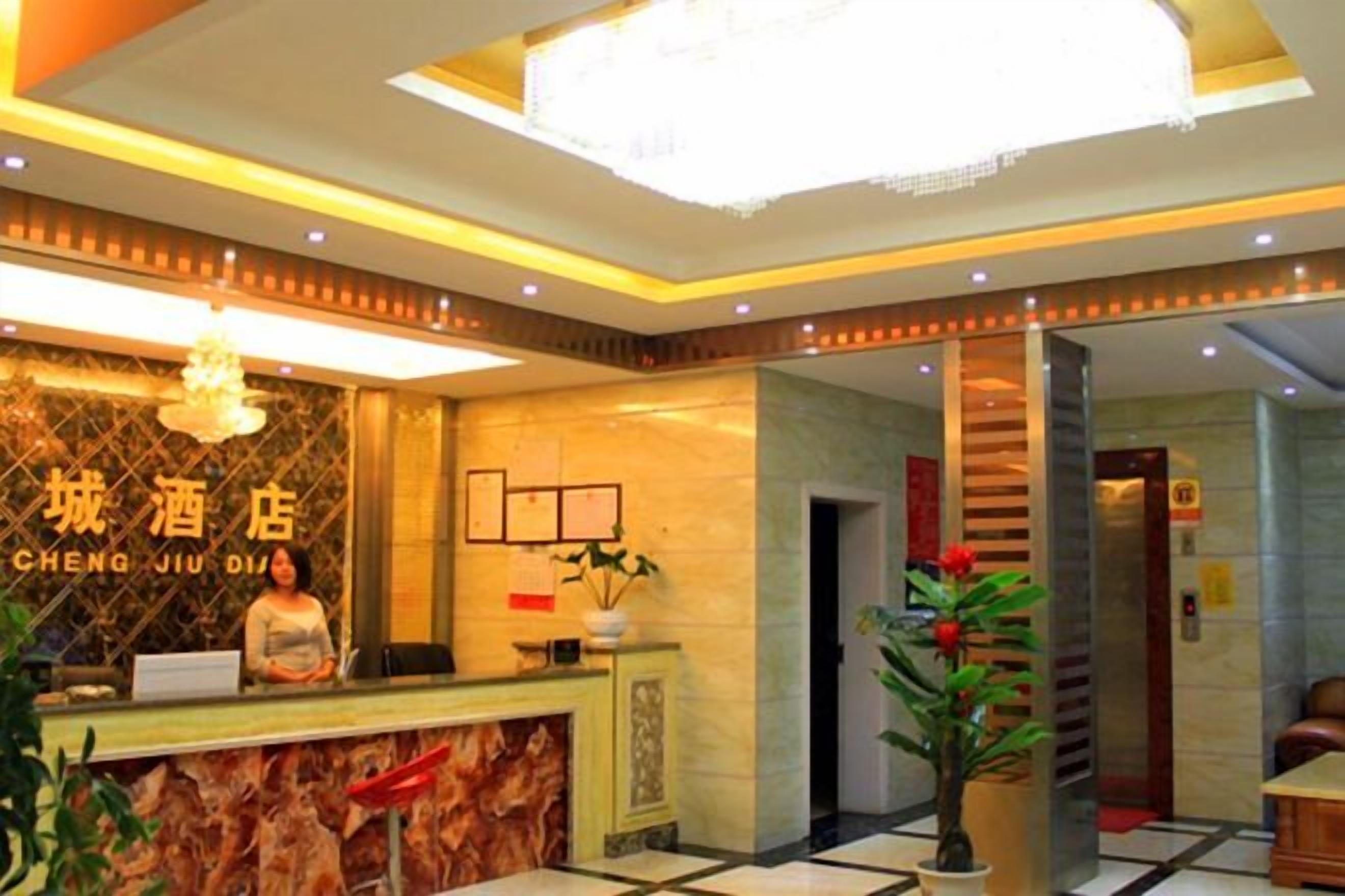 A hotel reception area with a reception desk, a chandelier, and a plant.