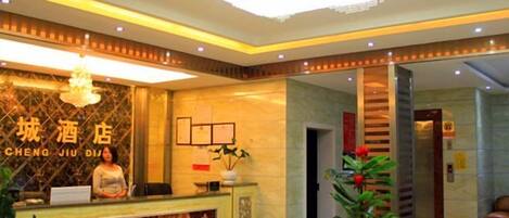 A hotel reception area with a reception desk, a chandelier, and a plant.