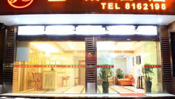 Un hotel con un llamativo letrero rojo y amarillo, una zona de recepción con sofá y plantas, y una entrada visible.