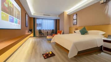 A hotel room with a bed, a desk, a chair, a TV screen, and a projector.
