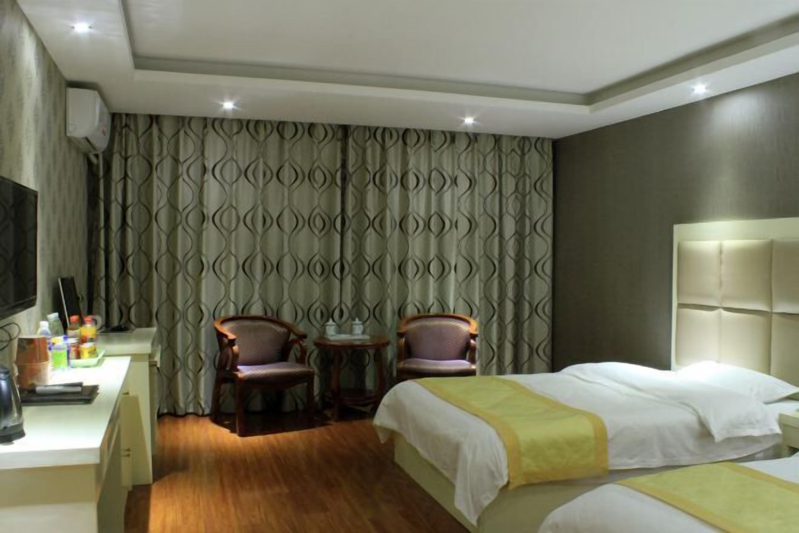 A hotel room with two beds, a desk with a chair, a television, and a patterned curtain.
