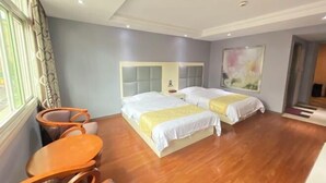 Habitación de hotel con dos camas, piso de madera, una mesita y un ventanal con cortinas.