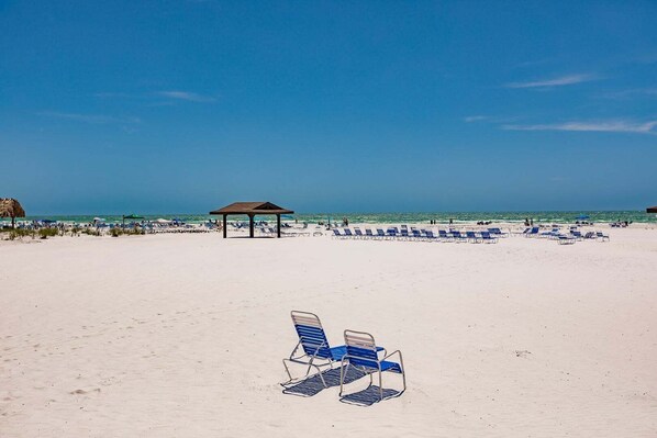 A beach with a pavilion and rows of blue lounge chairs.