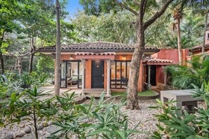 Uma casa com telhado de telhas, porta preta e jardim com diversas plantas.