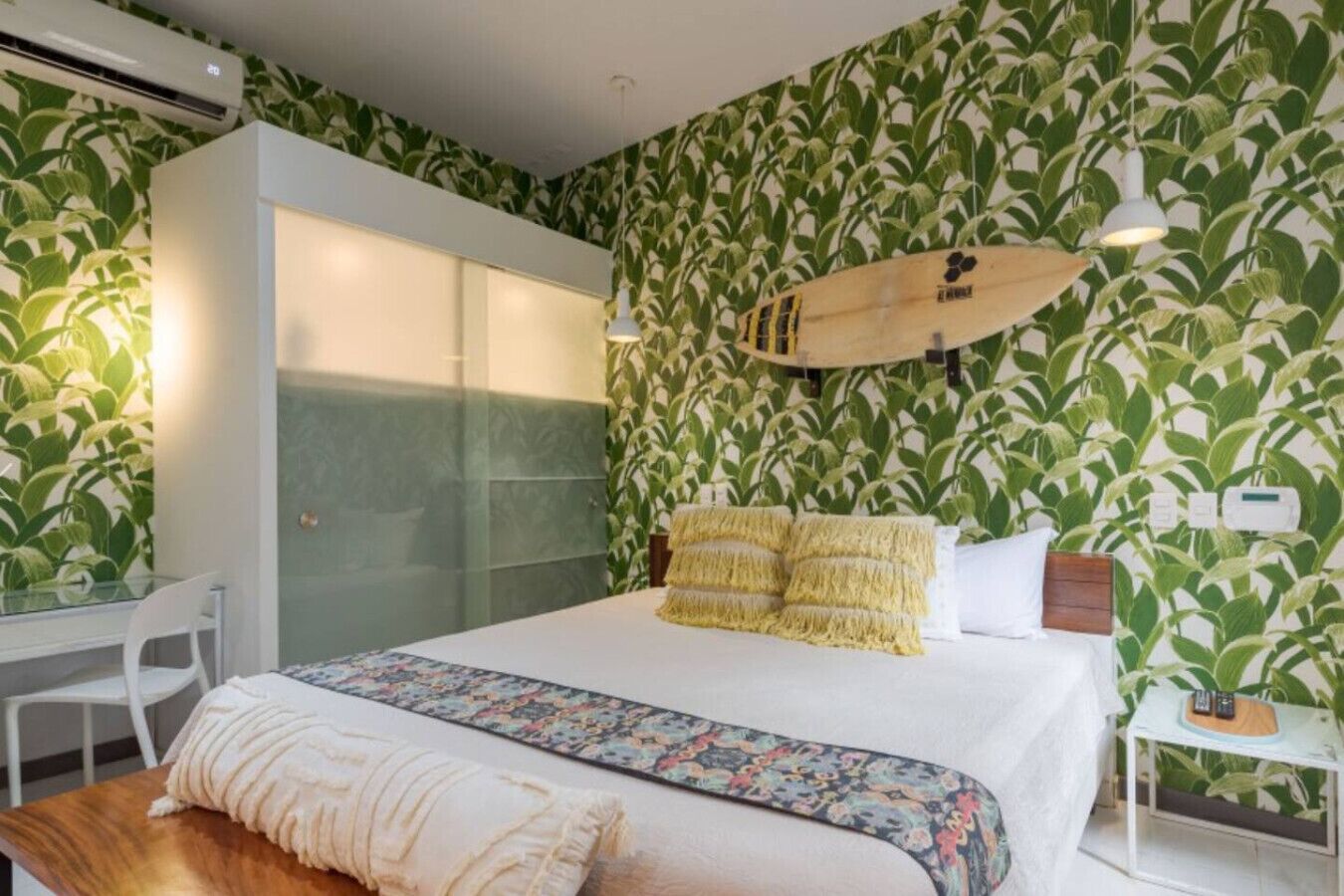 A bedroom with a bed, a bedside table, a chair, and a wall with a leafy pattern.