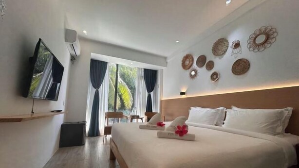 A modern hotel room with a large bed, a flat-screen TV, a small seating area, and decorative wall art. - Fun Hotel (Panglao Municipality)