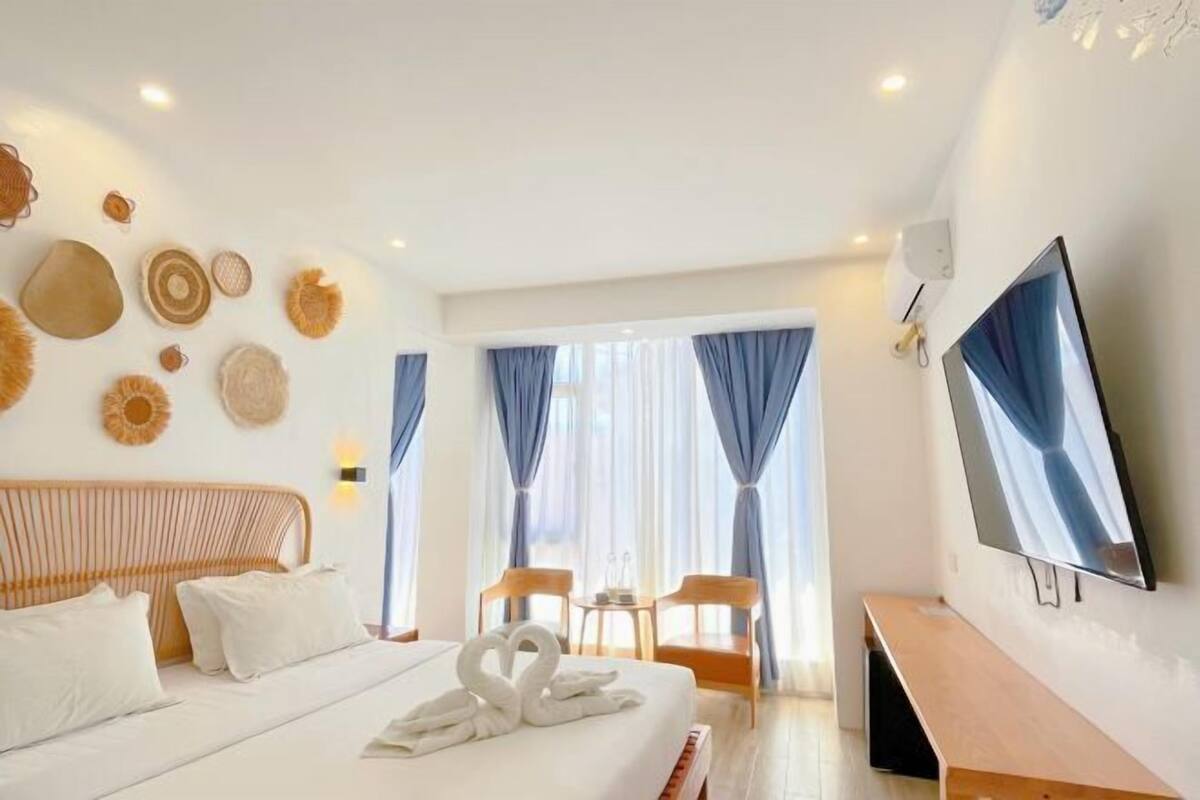 A hotel room with a bed, a TV, a desk, and a window with curtains.