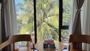 A room with two wooden chairs, a small round table with a decorative item, and a window with a view of palm trees. - Fun Hotel (Panglao Municipality)