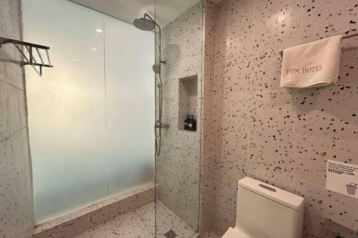 A modern bathroom with a glass-enclosed shower, a toilet, and a towel rack with a "FUN HOTEL" sign.