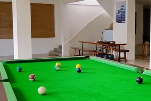 Ein Billardtisch mit Kugeln in einem Raum mit einer Treppe und einem Tisch mit Gegenständen darauf.