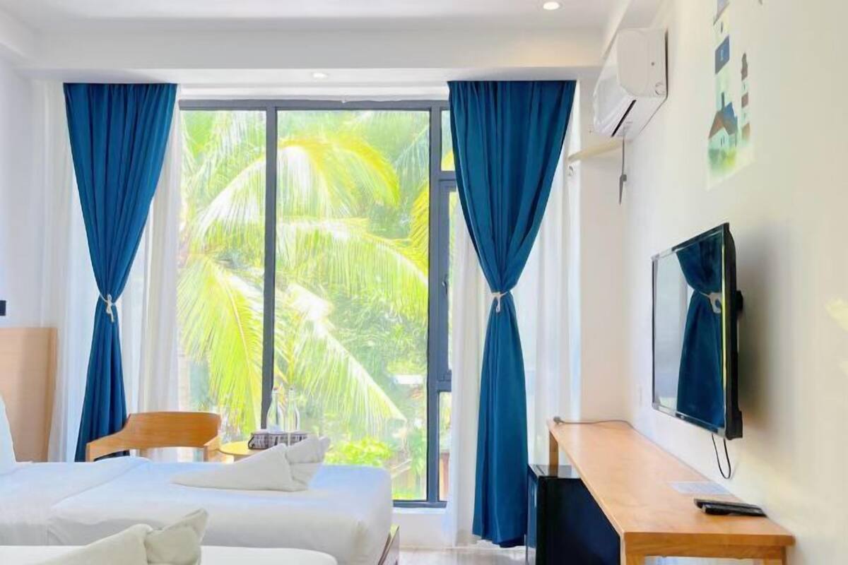 A hotel room with a bed, a desk, a TV, and a large window with curtains.