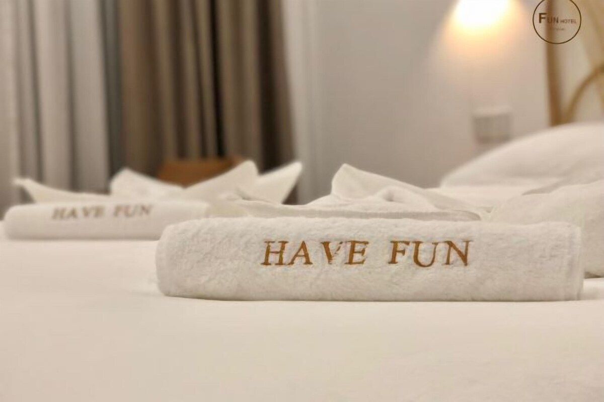 A hotel room with neatly folded towels on the bed, each with 'HAVE FUN' embroidered on them.