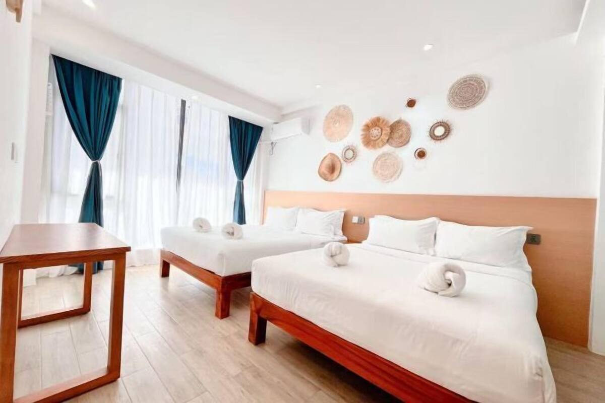 A hotel room with two beds, a wooden table, and a wall decorated with woven hats.